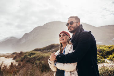 Loving couple standing outdoors at the beach and looking at a view. Caucasian man and woman in warm clothing at the seashore. - JLPSF03091