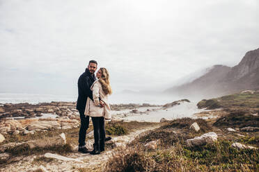 Young man and woman standing together at the beach in winter wear. Couple at the seaside during winter vacation. - JLPSF03097