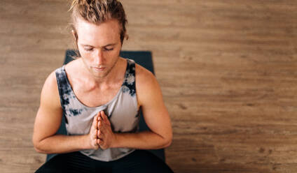 Overhead-Ansicht von fit junger Mann Praxis Yoga sitzen auf dem Boden mit seinen Händen verbunden. Fitness Kerl tun Yoga-Meditation drinnen. - JLPSF03105