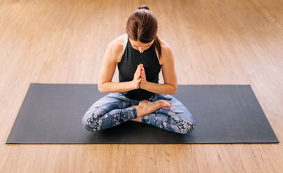 High angle view of young woman working out at home, doing yoga exercise on mat. Female sitting half Lotus pose. Ardha padmasana yoga pose. - JLPSF03131