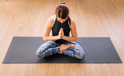 Hohe Winkel Ansicht der jungen Frau arbeiten zu Hause, tun Yoga-Übung auf Matte. Weibliche sitzende Hälfte Lotus-Pose. Ardha padmasana Yoga-Pose. - JLPSF03131