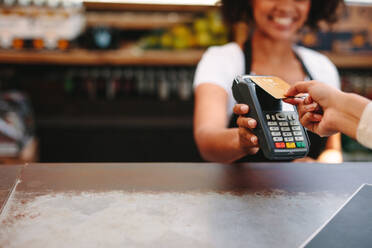 Kunde, der drahtlos oder kontaktlos mit Kreditkarte bezahlt. Lächelnde Kassiererin, die die Zahlung über NFC-Technologie akzeptiert. - JLPSF03140