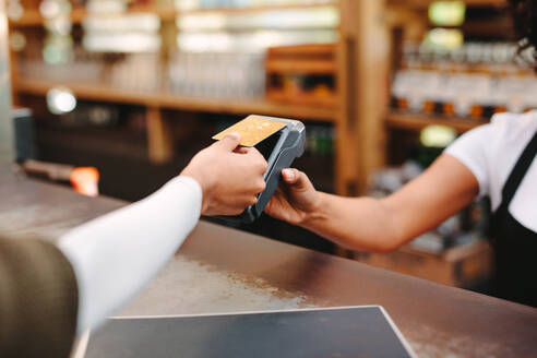 Ein Kunde, der mit seiner Kreditkarte drahtlos oder kontaktlos bezahlt, und ein Angestellter im Geschäft, der die Zahlung über die NFC-Technologie akzeptiert. - JLPSF03141