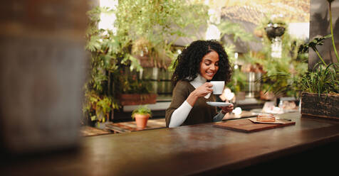 Lächelnde Frau, die an einem Tisch sitzt und eine Kaffeetasse in der Hand hält. Frau sitzt im Freien und frühstückt in einem Café - JLPSF03152