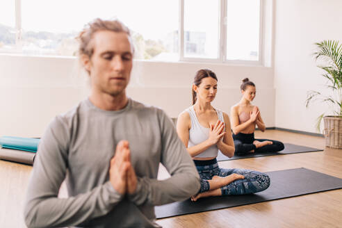 Frau übt Yoga in der Turnhalle Klasse mit Menschen sitzen um. Menschen in Lotus-Pose meditieren, während im Raum sitzen. - JLPSF03153