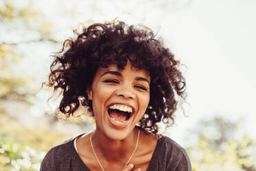 Close up of young woman with curly hair laughing. Woman standing in morning sun in cheerful mood. - JLPSF03173