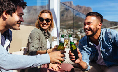 Eine Gruppe von Freunden stößt auf einer Dachterrassenparty mit Bier an. Junge Männer und Frauen hängen auf einer Dachterrassenparty ab und genießen Getränke. - JLPSF03179