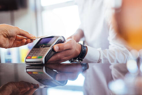 Hand eines Kunden, der mit einer kontaktlosen Kreditkarte mit NFC-Technologie bezahlt. Barkeeper mit einem Kreditkartenlesegerät am Bartresen mit einer Frau, die eine Kreditkarte hält. Fokus auf die Hände. - JLPSF03184