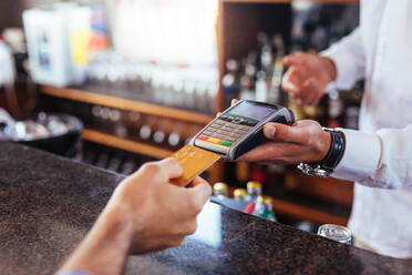 Customer making payment using credit card. Close up of card payment being made between customer and bartender in cafe. - JLPSF03185