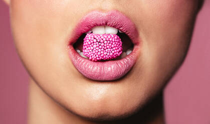 Schöne rosa Lippen mit einem Stück Süßigkeit. Nahaufnahme einer jungen Frau mit Süßigkeit im Mund. - JLPSF03199