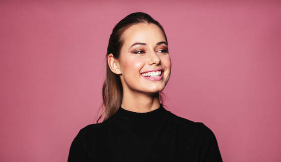 Portrait of caucasian female model standing and smiling against pink background. Beautiful woman with perfect skin and makeup looking away. - JLPSF03202