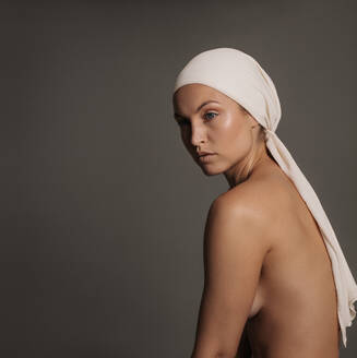 Aufnahme einer nackten Frau mit natürlichem Make-up auf grauem Hintergrund. Elegantes weibliches Modell posiert nackt mit Kopftuch. - JLPSF03208