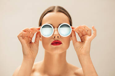 Nahaufnahme einer schönen Frau mit Sonnenbrille und roten Lippen vor beigem Hintergrund. Kaukasisches weibliches Modell mit Brille. - JLPSF03267