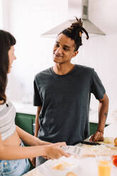 Zwei junge Verliebte kochen zusammen in einem Haus. Ausschnitt aus einem liebevollen jungen Paar, das sich fröhlich unterhält, während es in seiner Küche zu Hause Essen zubereitet. - JLPSF03285