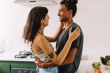 Affectionate young couple sharing a moment together at home. Shot of a happy young couple smiling affectionately while embracing each other in their kitchen. - JLPSF03289