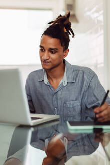 Businessman attending an online meeting while sitting alone. Focused young businessman making notes while on a virtual business meeting at home. Man taking a video call at his home office desk. - JLPSF03295