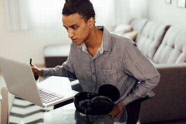 Geschäftsmann, der tagsüber von zu Hause aus arbeitet. Aufnahme eines konzentrierten jungen Geschäftsmannes, der einen Laptop benutzt, um seine Arbeit zu erledigen, während er allein an seinem Schreibtisch im Heimbüro sitzt. - JLPSF03298