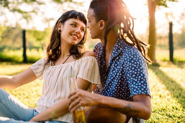 Verliebtes Paar, das einen romantischen Moment bei einer Verabredung verbringt. Zwei romantische junge Verliebte, die einander liebevoll anlächeln, während sie tagsüber in einem Park zusammensitzen. - JLPSF03313