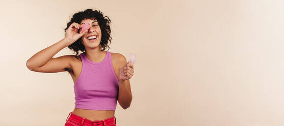 Fröhlich lächelnde junge Frau, die eine Menstruationstasse und eine Menstruationsscheibe in der Hand hält. Moderne Frau, die sich für nicht wegwerfbare und umweltfreundliche Hygieneprodukte für ihre weibliche Hygiene entscheidet. - JLPSF03350