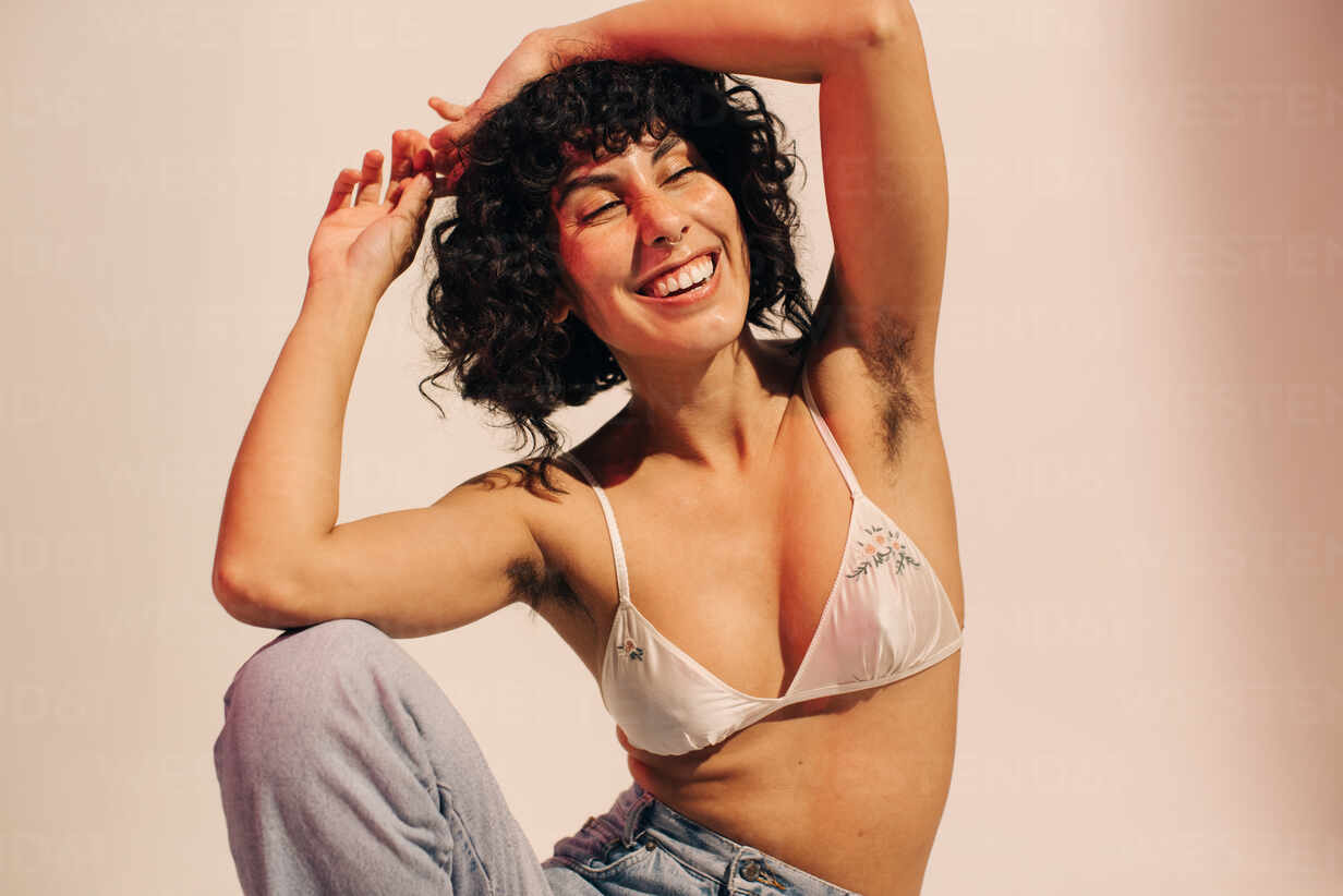 https://us.images.westend61.de/0001723282pw/unshaven-young-woman-smiling-cheerfully-while-wearing-a-bra-and-jeans-happy-young-woman-embracing-her-natural-body-and-underarm-hair-body-positive-young-woman-making-her-own-choice-about-her-body-JLPSF03410.jpg