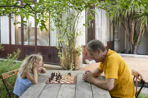 Granddaughter and grandfather enjoying chess in garden - SVKF00595