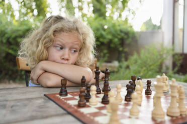 Nachdenkliches Mädchen mit blondem Haar betrachtet das Schachbrett auf dem Tisch - SVKF00596