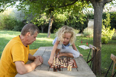 Enkelin spielt Schach mit Großvater im Garten - SVKF00604