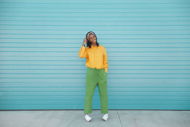 Smiling young woman standing in front of blue wall - PCLF00062