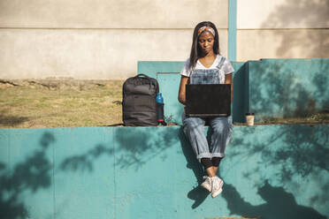 Young freelancer using laptop sitting on wall - PCLF00082