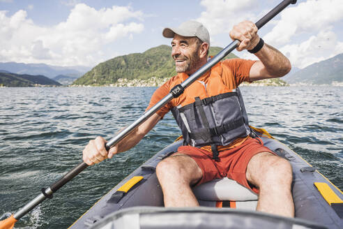 Lächelnder reifer Mann beim Kajakfahren auf einem See an einem sonnigen Tag - UUF27492