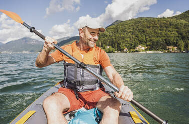 Lächelnder Mann beim Kajakfahren auf einem See an einem sonnigen Tag - UUF27494