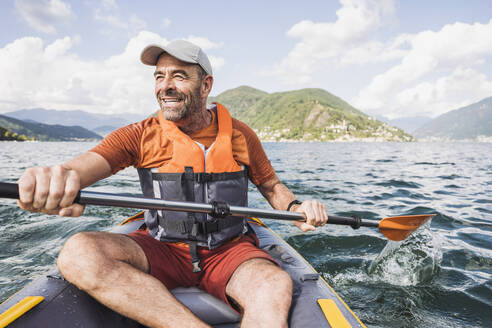 Happy mature man enjoying rowing kayak boat on sunny day - UUF27498