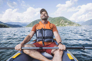 Mature man with eyes closed relaxing on kayak boat - UUF27501