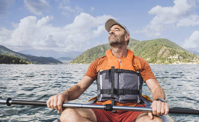 Smiling man with eyes closed sitting in kayak holding paddles - UUF27502