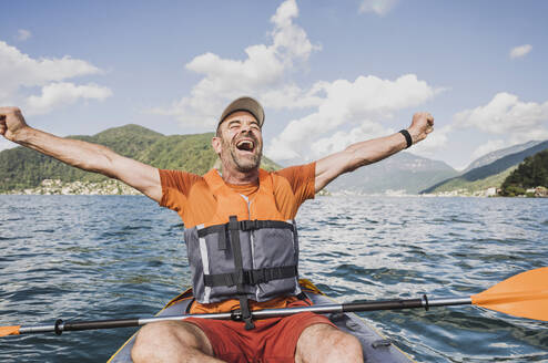 Excited mature man screaming with arms outstretched on lake - UUF27504