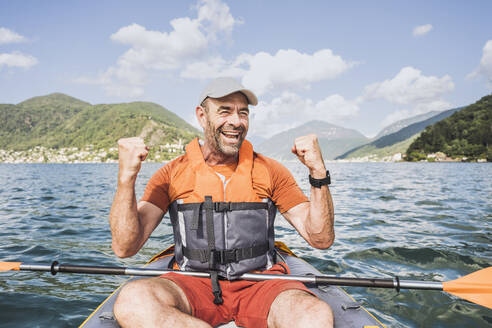 Happy mature man gesturing fists enjoying in kayak - UUF27506