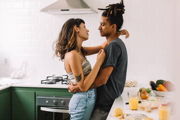 Interracial couple sharing a romantic moment together at home. Shot of an affectionate young couple embracing each other while standing together in their kitchen. - JLPSF03453