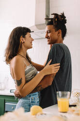 Romantic young couple sharing a moment together at home. Shot of a happy young couple smiling affectionately while embracing each other in their kitchen. - JLPSF03454