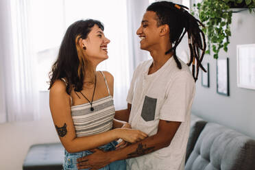 Junges Paar genießt die Gesellschaft des anderen zu Hause. Zwei liebevolle junge Liebende lachen, während sie tagsüber zusammen in ihrem Wohnzimmer stehen. - JLPSF03491