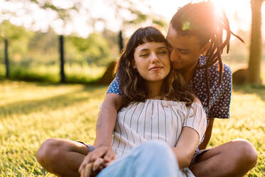 Gemütliches junges Paar, das sich umarmt, während es im Freien sitzt. Zwei junge romantische Liebende, die tagsüber in einem Park Zeit miteinander verbringen. - JLPSF03498