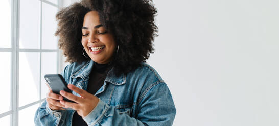 Lächelnde Frau, die ihr Mobiltelefon benutzt. Frau in Jeansjacke liest eine Textnachricht auf einem Smartphone. - JLPSF03556