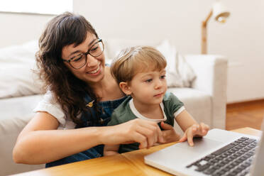 Lächelnde Frau und Sohn mit Laptop im Wohnzimmer. Kleiner Junge mit Mutter zu Hause am Laptop. - JLPSF03563