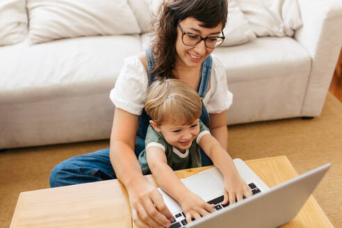 Junge mit Mutter, die sich zu Hause amüsieren. Lächelnde Frau und Sohn mit Laptop im Wohnzimmer. - JLPSF03569