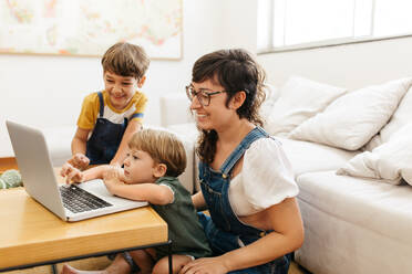 Mother and her children using a laptop computer at home. Family of three using laptop while sitting in living room. - JLPSF03574