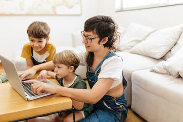 Mother showing something interesting on laptop to her kids. Mother and boys looking at something interesting on laptop computer in living room. - JLPSF03576