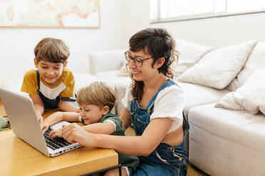 Kleiner Junge, der zu Hause mit seiner Mutter und seinem Bruder am Laptop lernt. Die Familie hat Spaß bei der Benutzung des Laptops. - JLPSF03577