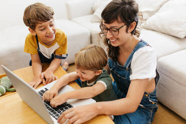 Lächelnde Frau mit ihren Kindern bei der Benutzung eines Laptops. Kinder genießen das Lernen am Laptop mit ihrer Mutter zu Hause. - JLPSF03578