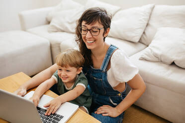Kleiner Junge mit Mutter, die sich zu Hause amüsieren. Lächelnde Frau und Sohn mit Laptop. - JLPSF03581