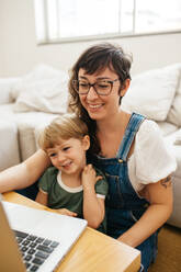 Smiling mother and son with laptop. Woman sitting with son looking at laptop and smiling. - JLPSF03582