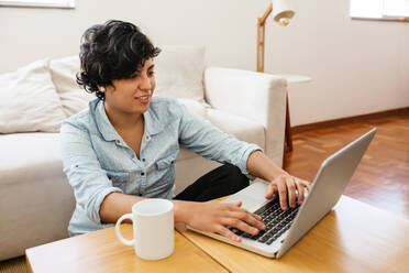 Woman sitting on floor and working on laptop. Female sitting at table with cup of coffee and using laptop. - JLPSF03589